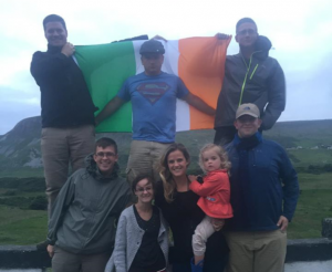 MMI Gaelic Club members, including Dr. Rankin Sherling, wife Claire, and Dr. Nicole Peacock., stand proudly alongside cadets displaying the Irish flag in the lush countryside.